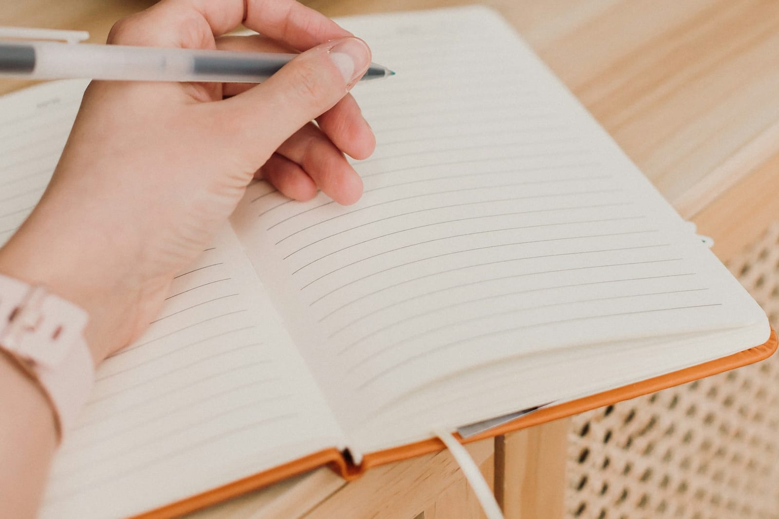 A hand with a pen over an open notebook, ready to write